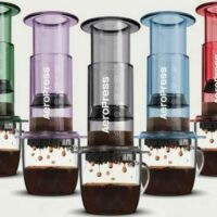 Cinq cafetières AeroPress colorées avec tasses remplies de café.