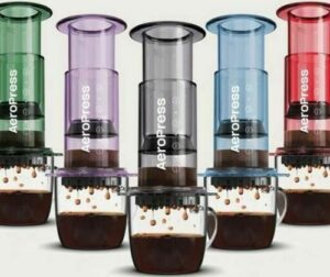 Cinq cafetières AeroPress colorées avec tasses remplies de café.